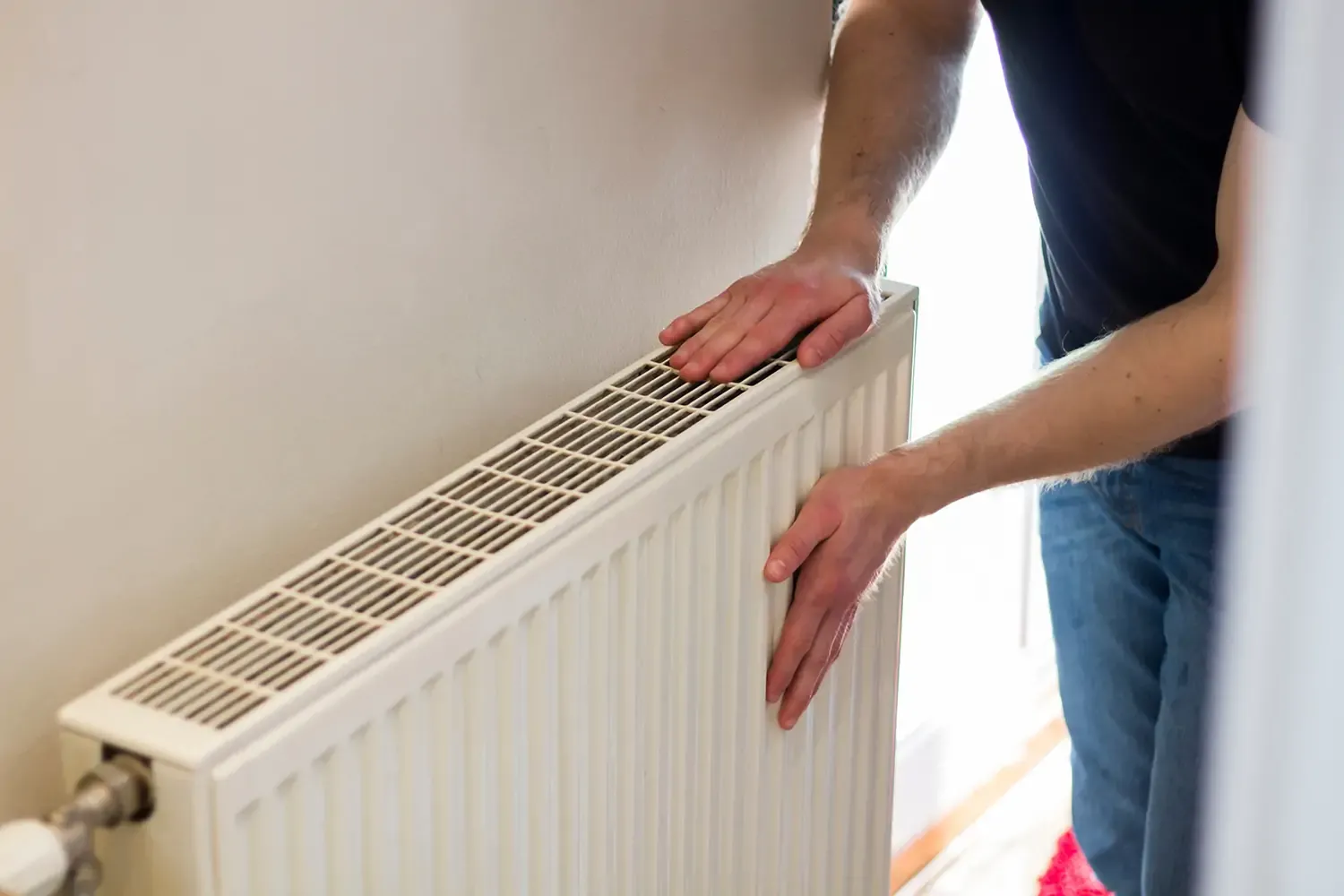 Man checking radiator warmth by hand to ensure efficient heating in a home
